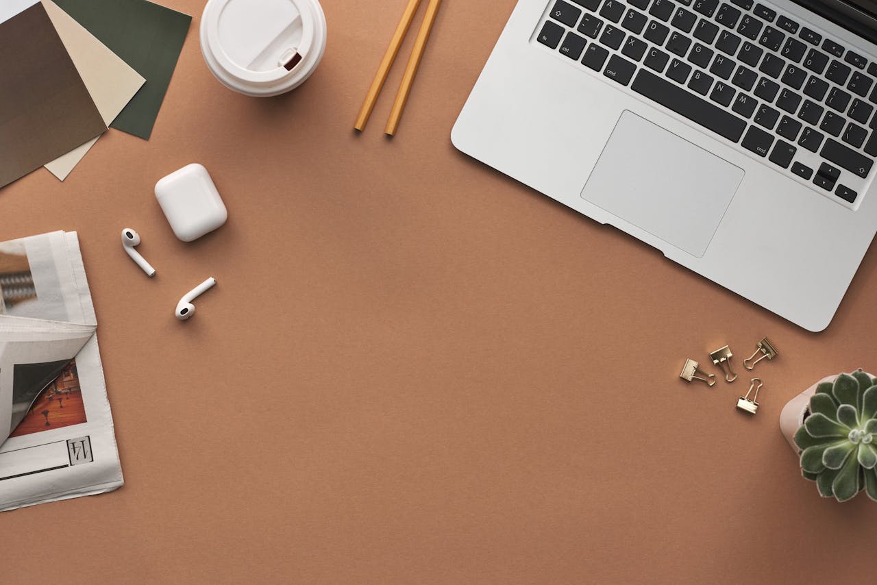 Flat lay of a modern workspace with a laptop, AirPods, and coffee for productivity.